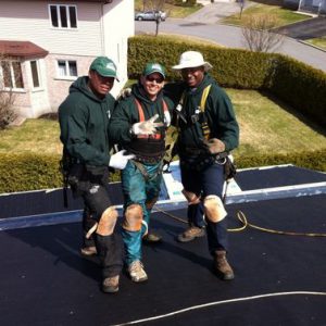 Three men standing on a roof with tools.